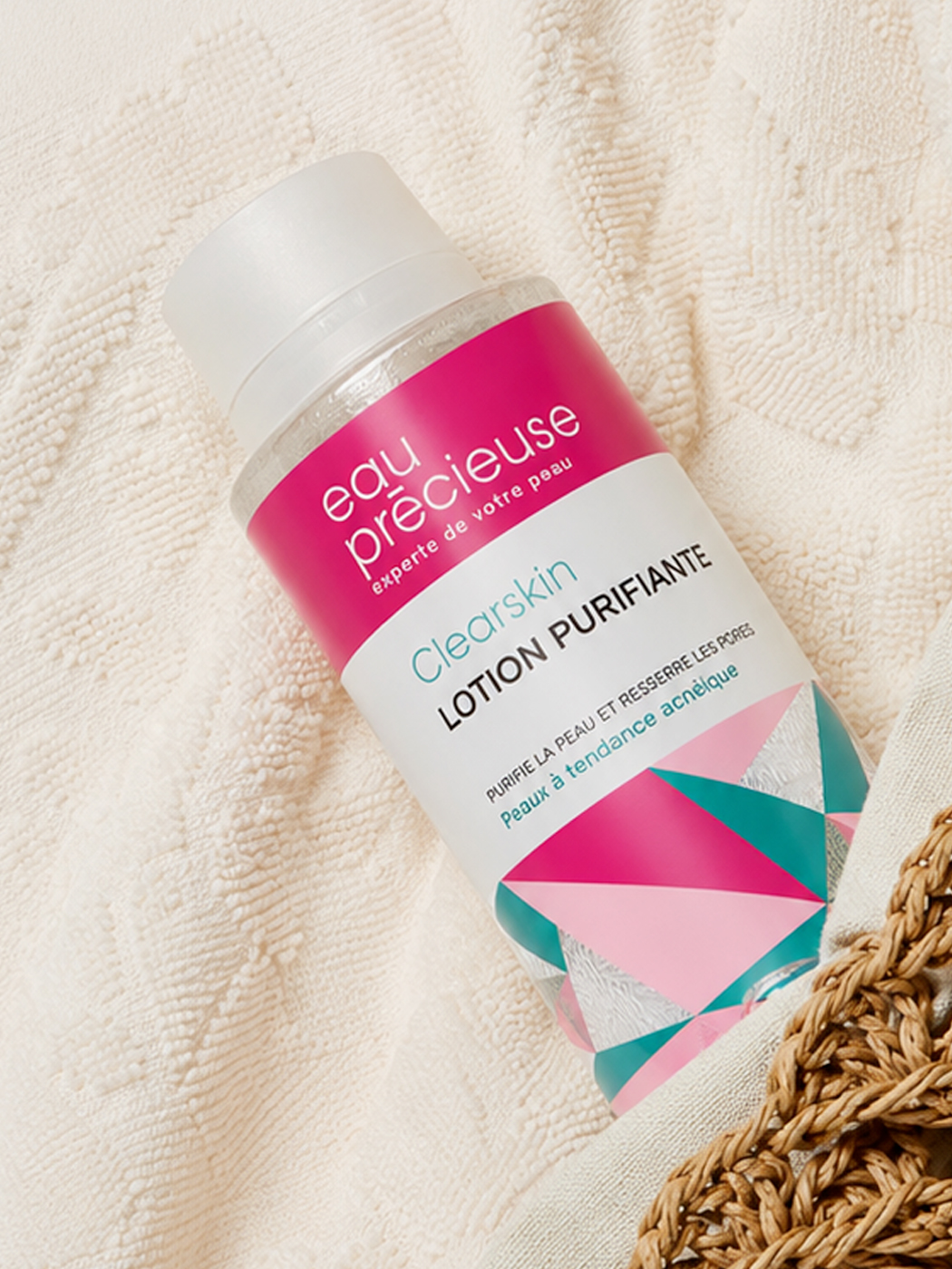 Flacon Eau Précieuse Clearskin posé à plat, motif géométrique rose et vert de l'édition spéciale