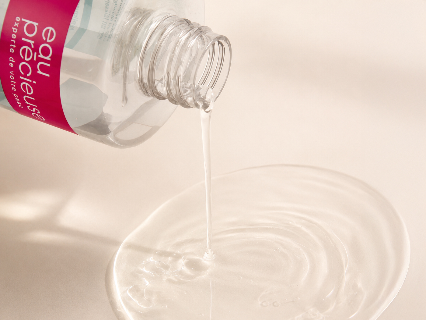Lotion Clearskin versée du flacon Eau Précieuse, formant une flaque transparente