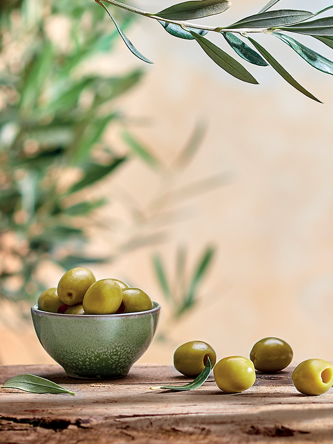Bol d'olives vertes sur une planche de bois, sous une branche d'olivier